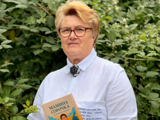 Eine Frau steht vor einer grünen Ecke. Sie hält ein Buch in der Hand.