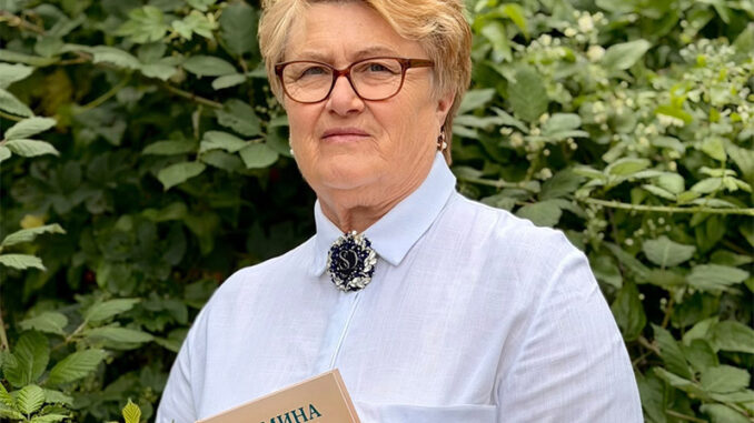 Eine Frau steht vor einer grünen Ecke. Sie hält ein Buch in der Hand.