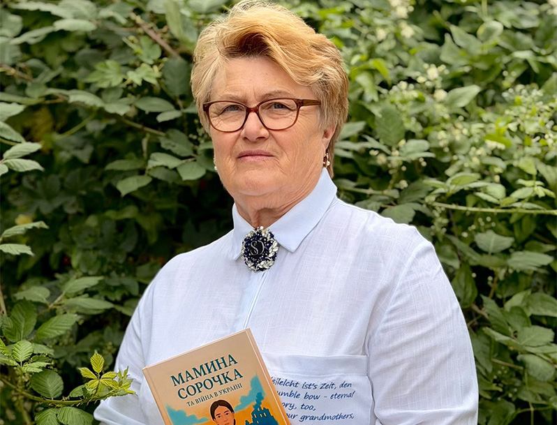 Eine Frau steht vor einer grünen Ecke. Sie hält ein Buch in der Hand.
